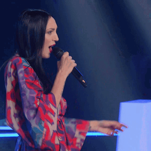 a woman singing into a microphone while wearing a floral dress