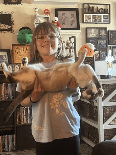 a girl holding a cat in front of a wall with a sign that says much