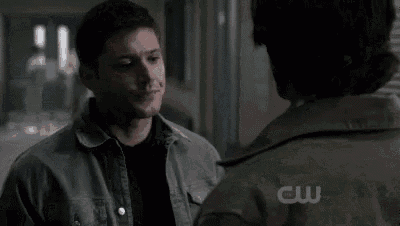 a man in a denim jacket is talking to another man in a white jacket in a hallway .