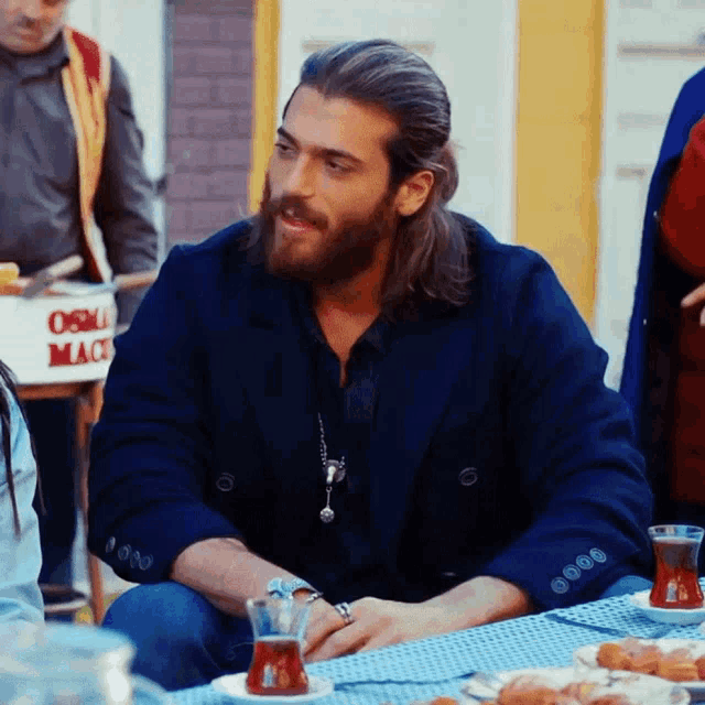 a man with long hair and a beard is sitting at a table in front of a box that says osma mace