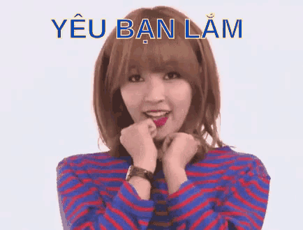 a girl in a blue and red striped shirt is making a funny face with the words yeu ban lam written above her
