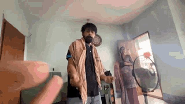 a man with a beard is dancing in a living room with a woman standing behind him .