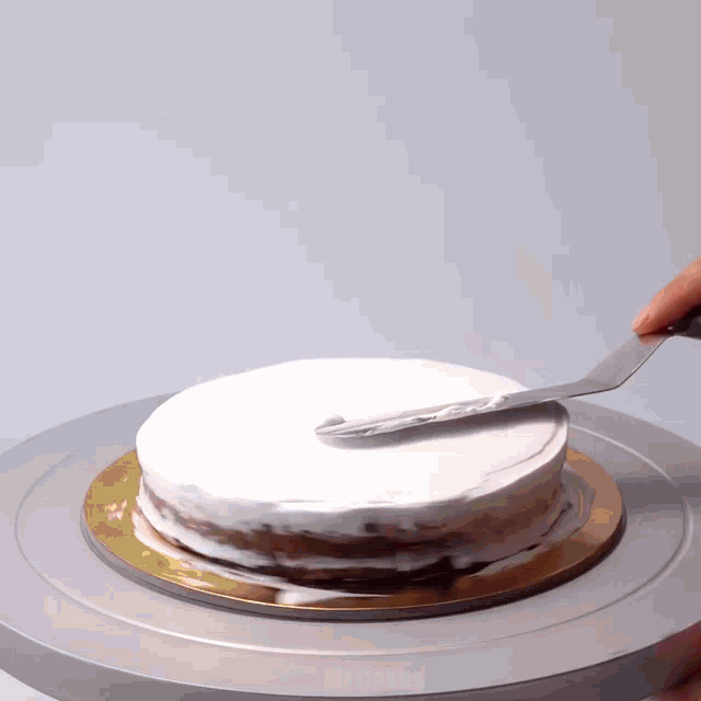 a person spreading frosting on a cake on a turntable