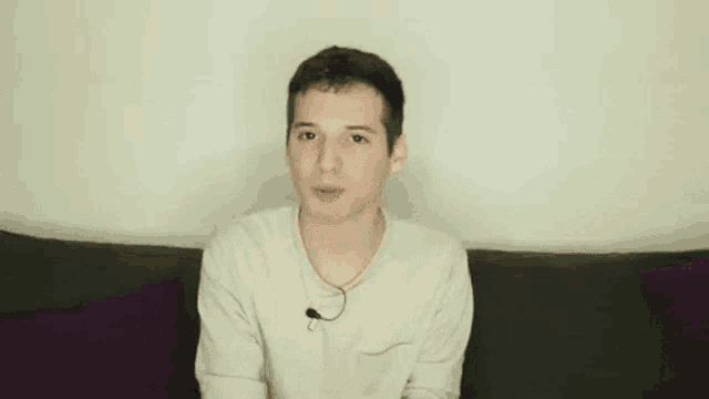 a young man is sitting on a couch making a funny face with his hands in the air .