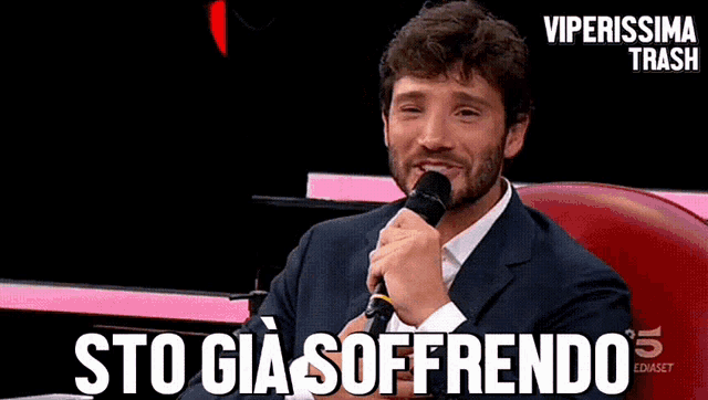 a man in a suit holds a microphone and says sto gia soffrendo
