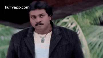 a man with a mustache and a necklace is wearing a black jacket and a white t-shirt .