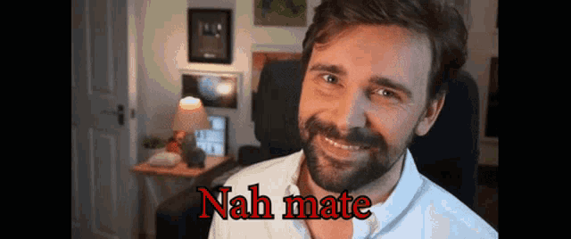 a man with a beard is smiling in front of a sign that says " nah mate "