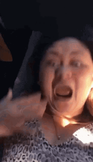 a woman in a leopard print shirt is making a funny face while sitting in a car .