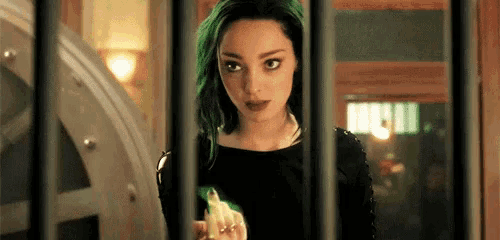 a woman with green hair is behind bars in a prison cell holding a green object .