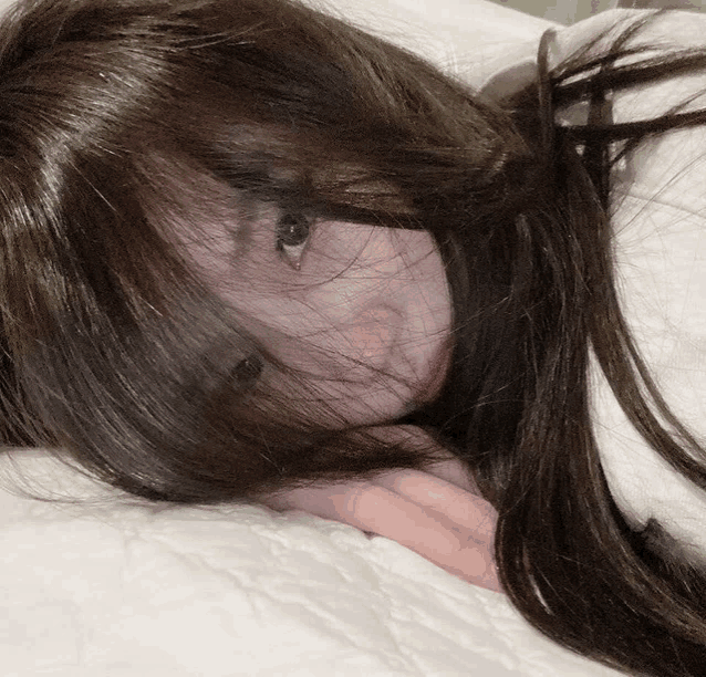 a close up of a woman laying on a bed with her hair covering her face