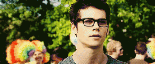 a young man wearing glasses and a gray shirt is standing in front of a crowd .