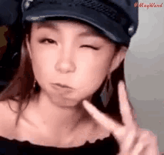 a woman wearing a hat is making a peace sign with her hand