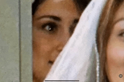 two women are peeking out from behind a wall .