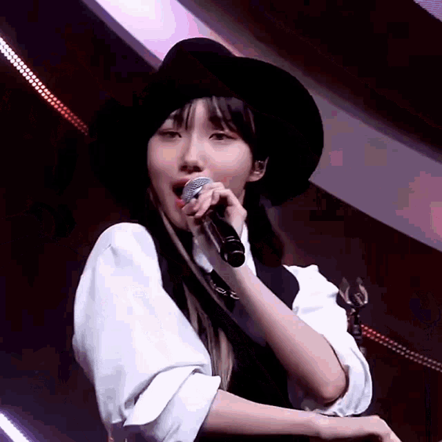 a woman is singing into a microphone while wearing a black hat .
