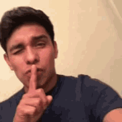 a man in a blue shirt is making a shhh sign with his finger .