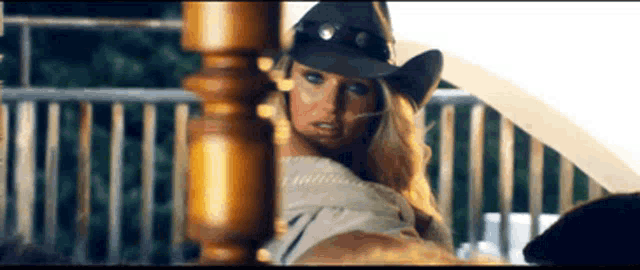 a woman wearing a cowboy hat is standing next to a wooden post