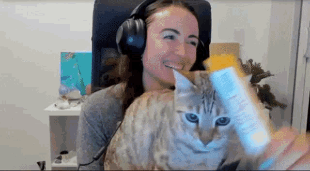 a woman wearing headphones is holding a cat and a remote control