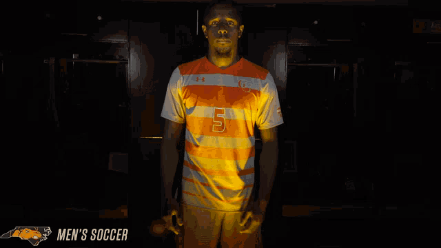 a man standing in a dark room with the word men 's soccer on the bottom right