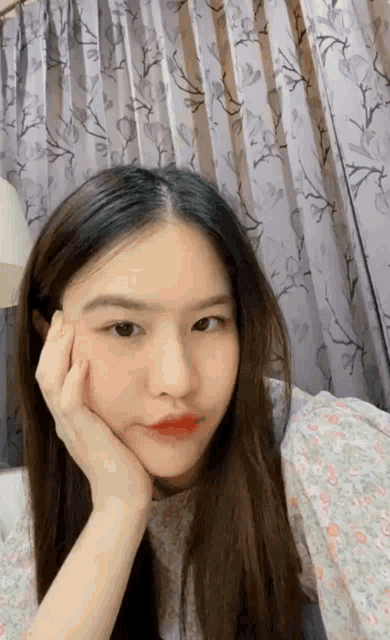 a girl with her hand on her face in front of a curtain
