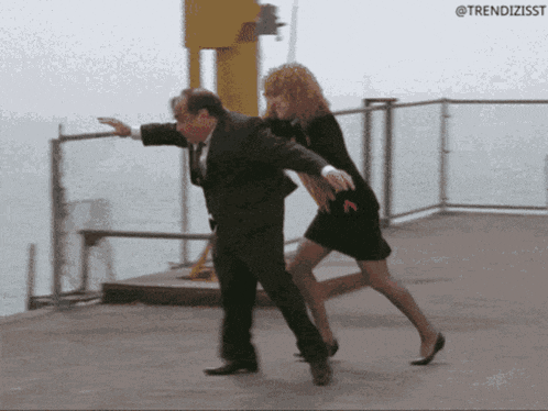 a man in a suit is holding a woman in a black dress who is running away