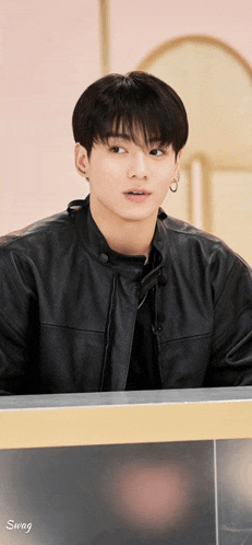a young man wearing a black leather jacket and earrings is sitting at a table