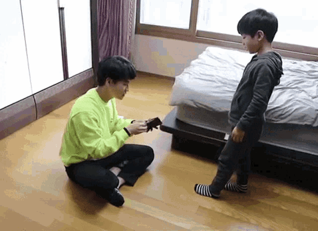 a man and a boy are sitting on the floor in a bedroom . the boy is holding a guitar .