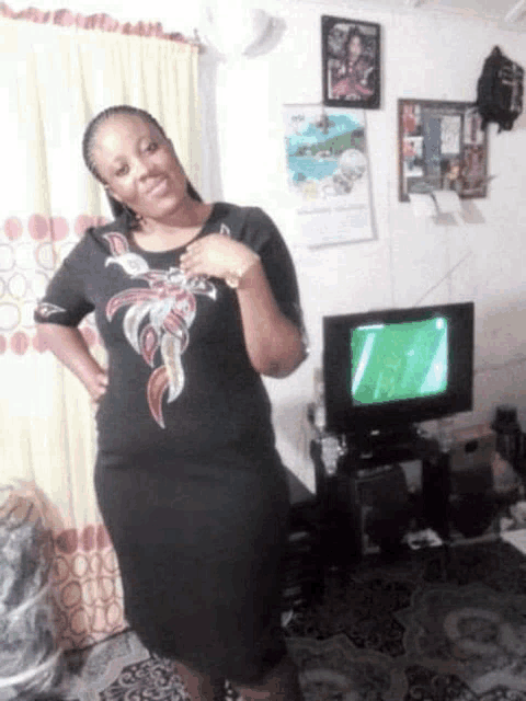 a woman in a black dress stands in front of a flat screen tv