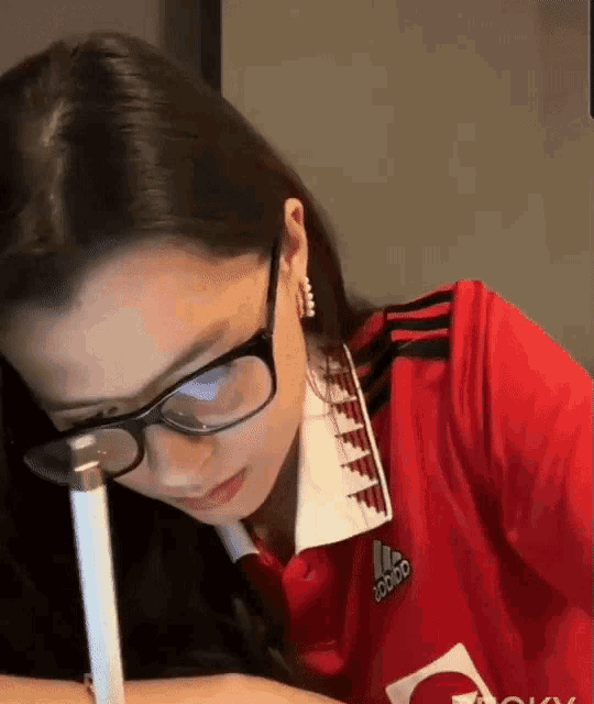 a woman wearing glasses and an adidas shirt looks down at something