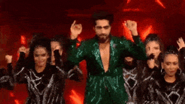 a man in a green sequined jacket is dancing with a group of women on a stage .