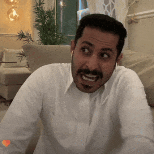 a man with a beard wearing a white shirt and ear buds looks at the camera