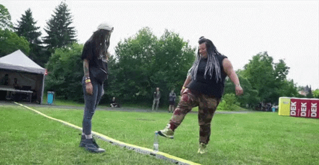 two women are standing on a tightrope in a field with a sign that says dek on it .