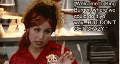 a woman in a red uniform is holding a hamburger and talking to a man in a restaurant .