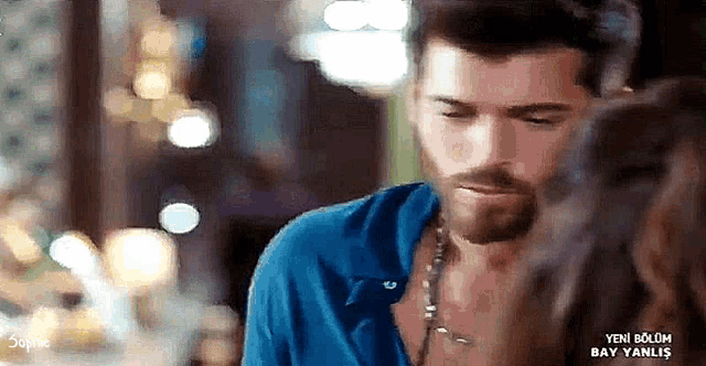 a man with a beard is looking at a woman with a necklace around his neck .