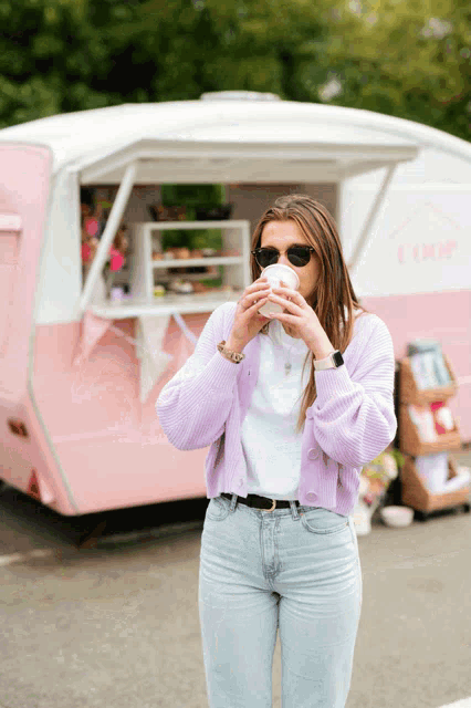 a woman drinking from a cup in front of a trailer that says drip