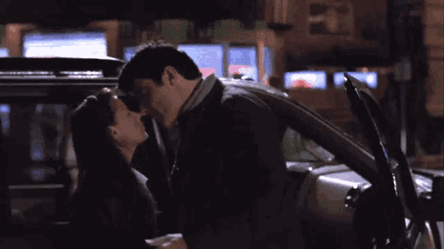 a man and woman are kissing in a car at night .