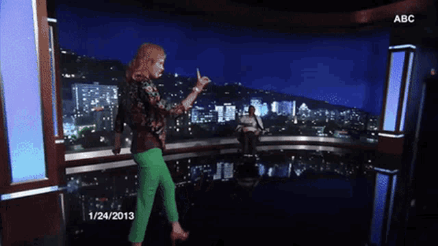 a woman in green pants stands in front of a screen that says abc on it