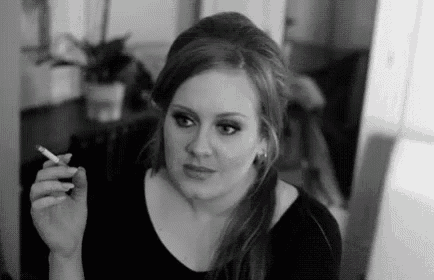 a woman is smoking a cigarette in a room in a black and white photo .