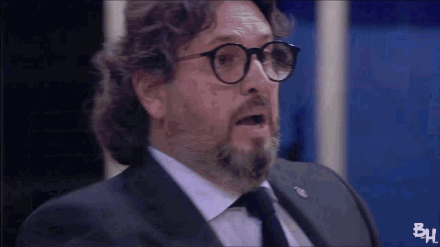 a man with glasses and a beard is wearing a suit and tie with bh written on the bottom