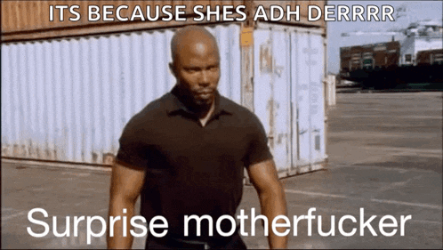 a man in a black shirt is standing in front of a shipping container with the words `` surprise motherfucker '' written on it .