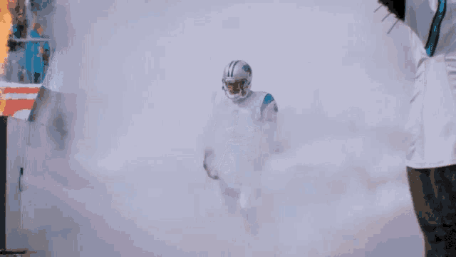 a football player in a carolina panthers uniform runs through smoke