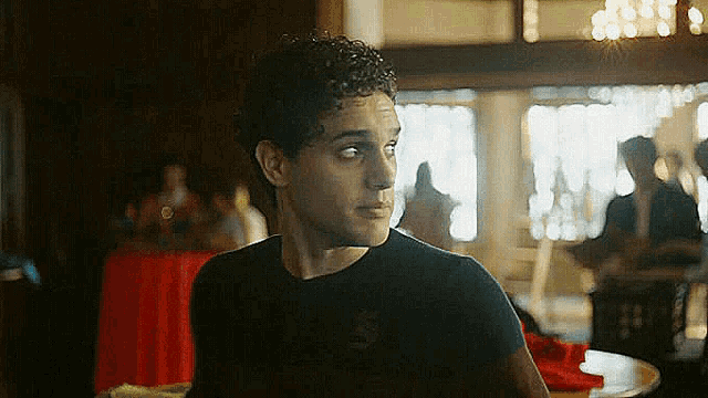 a man with curly hair is sitting at a table in a restaurant looking at the camera .