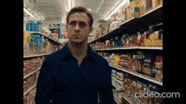 a man in a blue shirt stands in a grocery store aisle