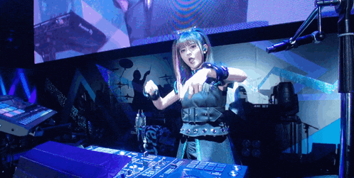 a girl with blue hair is standing in front of a dj mixer and giving a thumbs up