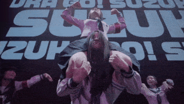 a woman is being carried on a man 's shoulders in front of a large suzuki sign