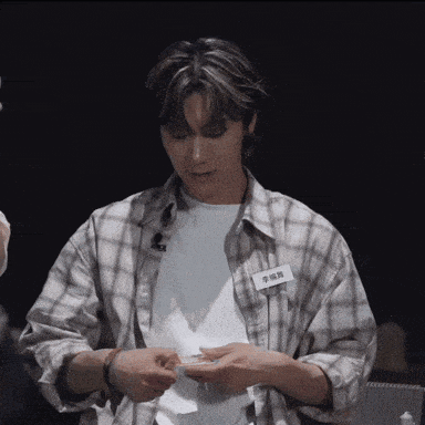a young man in a plaid shirt is holding a piece of paper in his hands .