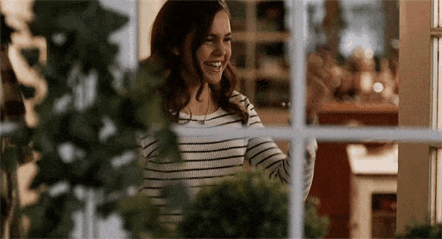 a woman in a striped shirt is standing in front of a window .