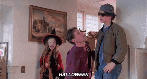a man in a bomber jacket is standing next to a girl in a witch costume and a boy in sunglasses .