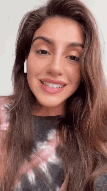 a woman wearing a tie dye shirt and earbuds smiles for the camera