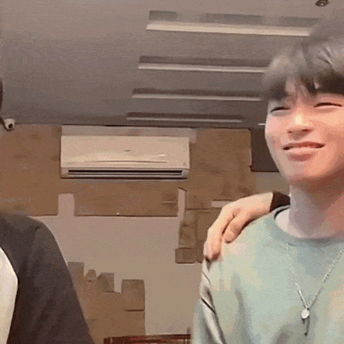 a man is smiling with his arm around another man 's shoulder in a room with boxes and an air conditioner .