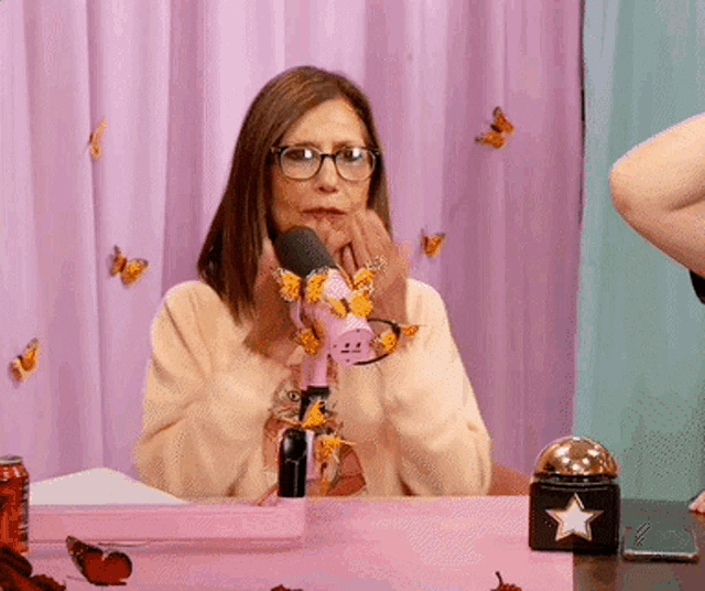 a woman wearing glasses is sitting in front of a pink microphone with butterflies on it